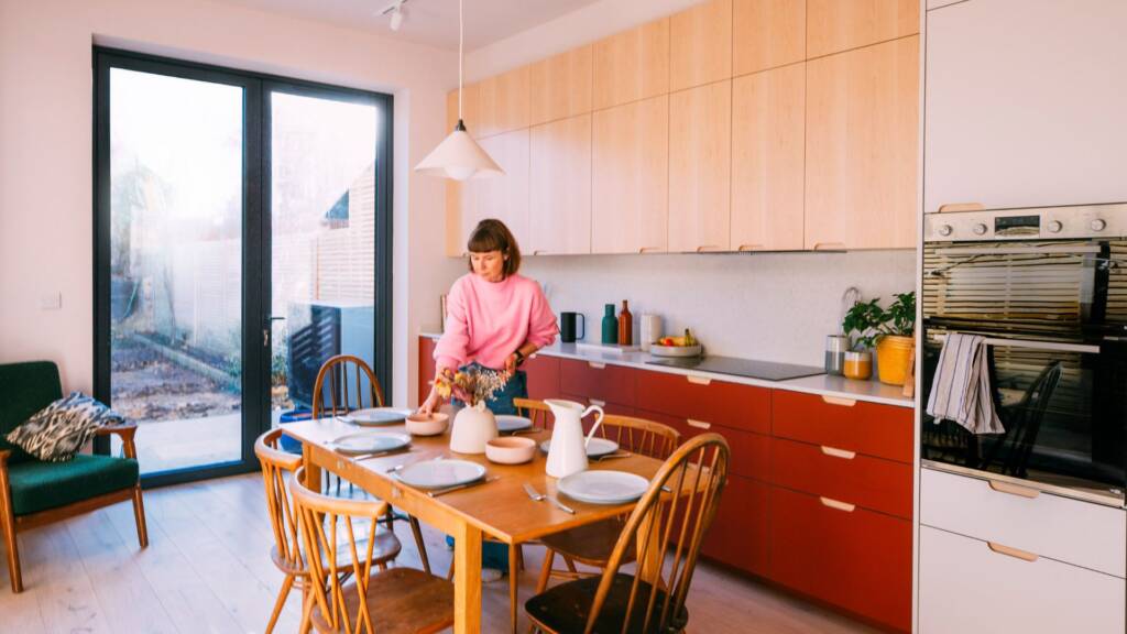 Alternate angle showing sunlit kitchen with red base cabinets, timber overhead units, white cabinets with encased oven.